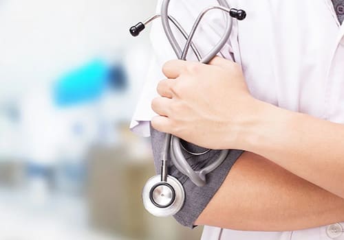 A doctor in a white coat holding a stethoscope against their arm.