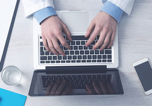 Overhead view of a person in a lab coat working on a laptop at a desk.