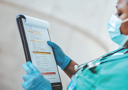 A medical professional in scrubs reads a clipboard with a checklist