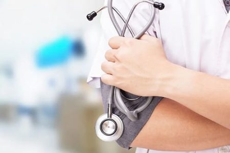 A doctor in a white coat holding a stethoscope against their arm. A doctor in a white coat holding a stethoscope against their arm.