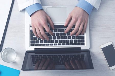 Overhead view of a person in a lab coat working on a laptop at a desk. Overhead view of a person in a lab coat working on a laptop at a desk.